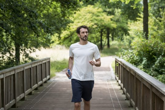 Mann joggt mit natürlichem Mineralwasser über eine Brücke