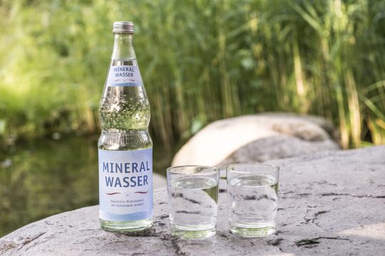 Mineralwasserflasche mit Gläsern auf einem Stein